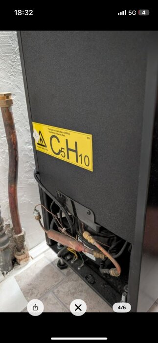 Kompressor med kopparrör och etikett "C5H10" i ett köldmediesystem, placerad nära en vägg.