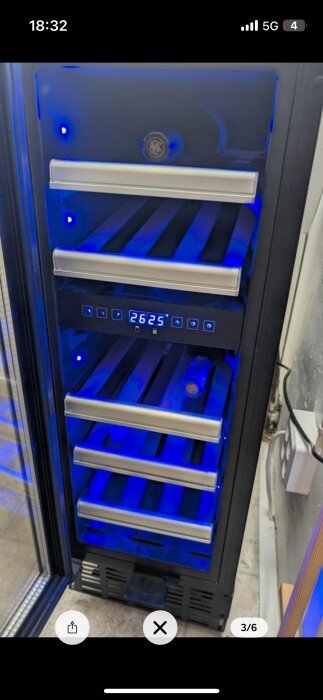 Vinkylskåp med blå belysning och digital display som visar 26.25 grader. Flera hyllor synliga, en innehåller en vinflaska.