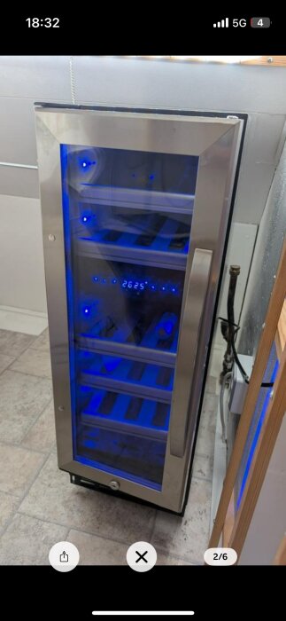 Ett större kylskåp med glasdörr, belyst med blått ljus och flera hyllplan synliga inuti. Digital display visar "2625".