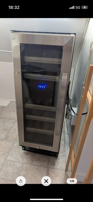 Vinkyl med glasdörr och digital display som visar "26.25". Står på klinkergolv nära en vägg.