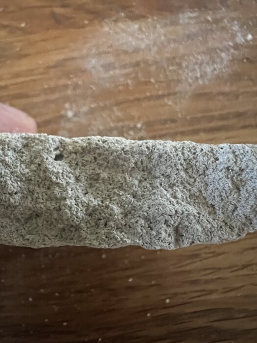 En nærbilde av en stykke av en grå murpuss med grov tekstur, ligger på en treoverflate.