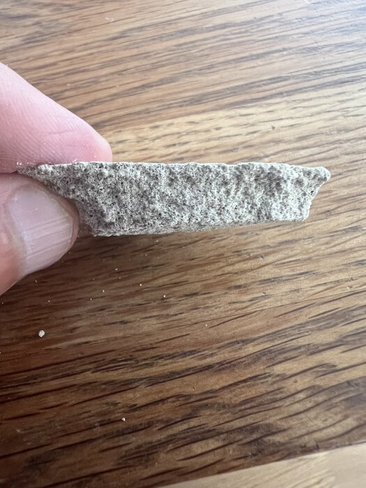 En bit av C-puts holdes mellom fingrene, viser tekstur og tykkelse mot en trebord.
