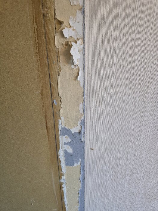 Avskalad tapet visar lager av blå och beige färg på masonitskiva; rätt verktyg behövs för borttagning.