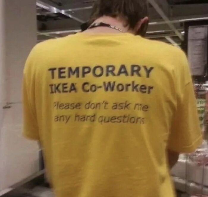 Person i gul T-shirt med texten "Temporary IKEA Co-Worker, Please don't ask me any hard questions" på ryggen, i en butiksinteriör.