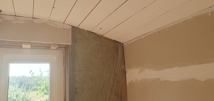 Rundad takhörna med synliga skivor och oavslutad gips, fönserkarm syns med utsikt utomhus. Fråga om hur man snyggt mäter och sätter taklist här.