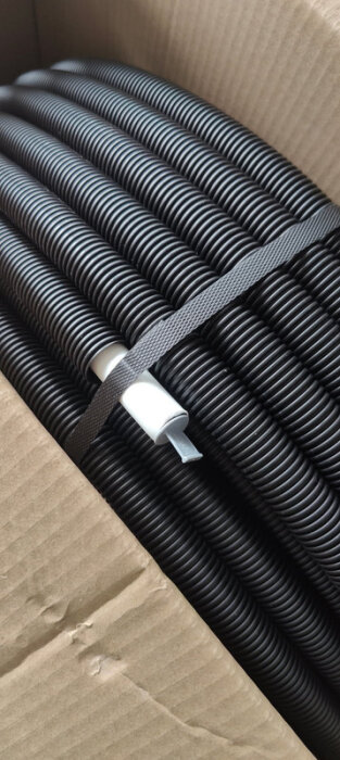 Svart korrugerat rör i en kartong, redo för grovkapning och montering av VVS-kopplingar.