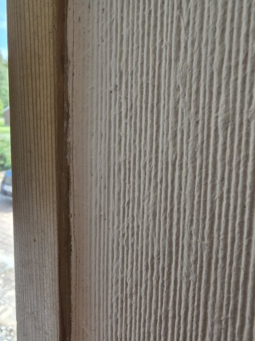 Grovt texturerad väggyta bredvid en träkarm.