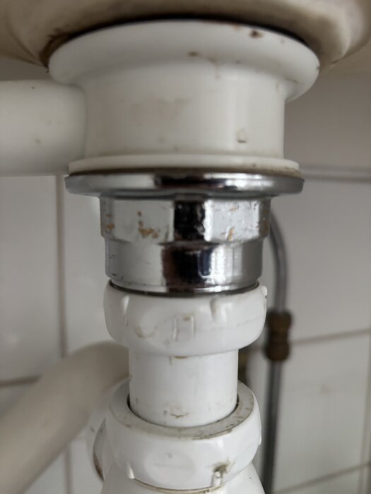 Bottenventilen i ett handfat visas underifrån, där den verkar fast. Vattenledning och del av avloppssystem syns där ventilen är placerad.