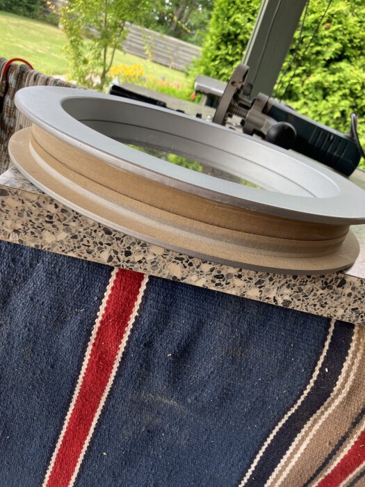 Rund trä- och metallram för fönstermontering, placerad på ett bord med en bordssåg och trädgård i bakgrunden.