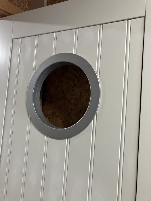Rund fönsteröppning på en vit innerdörr med slipade kanter och montering för glas.