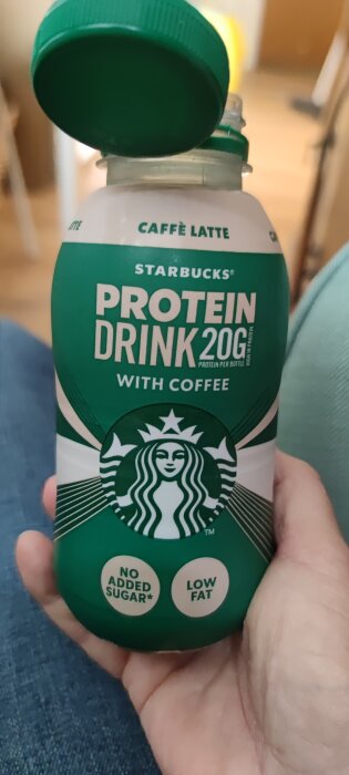 Grön flaska med Starbucks proteinshake, smak caffe latte, hÄlls i handen. InnehÄller 20g protein, inget tillsatt socker, lÄg fetthalt.