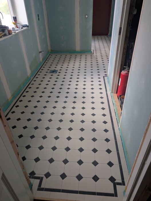 Ett nyrenoverat rum med svart-vit kaklad golvyta i ett geometriskt mönster och gröna väggar under uppbyggnad.