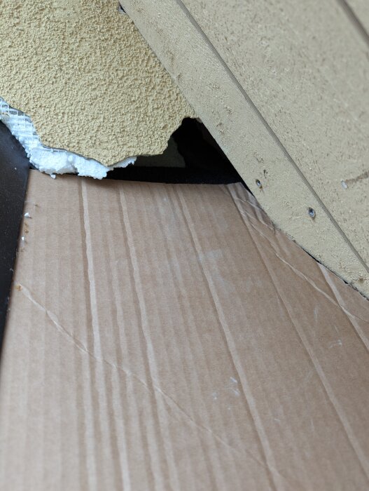 Hål i en vägg med synlig vit frigolit som saknas på en del av ytan, träpaneler syns runt hålet.