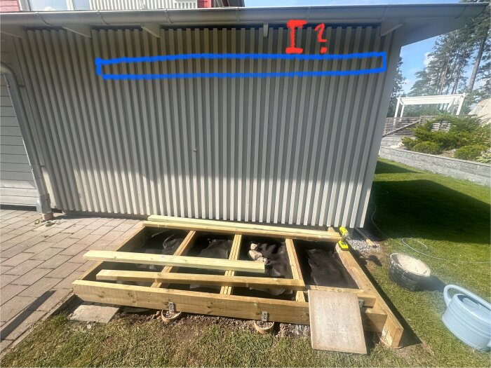 Byggarbetsplats med ny trästomme intill vit fasad, blå markering visar regelläge för kallförråd, röd fråga om marginal till tak.