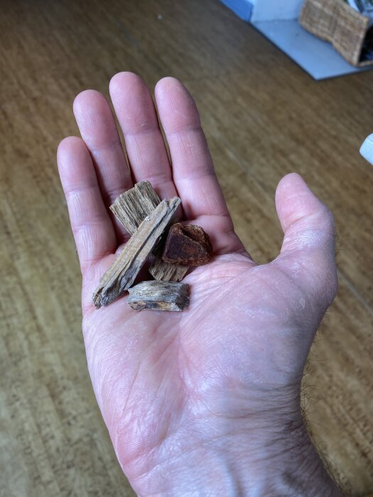 Hand som håller träflisor av olika storlekar, liggande på en träyta.