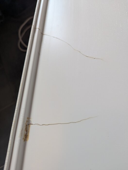 Spricka och lagning på vit badkarsfront; kräver spackling och färg.