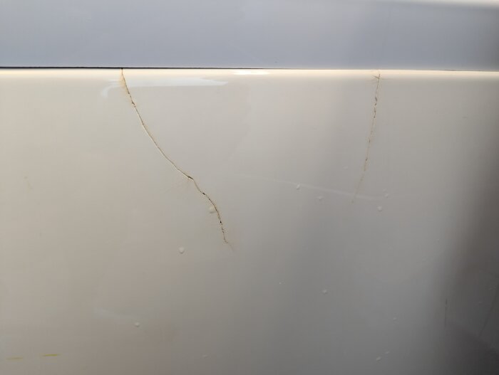 Spricka i badkarets frontpanel efter ihopsättning, behöver spackel och färg för reparation.