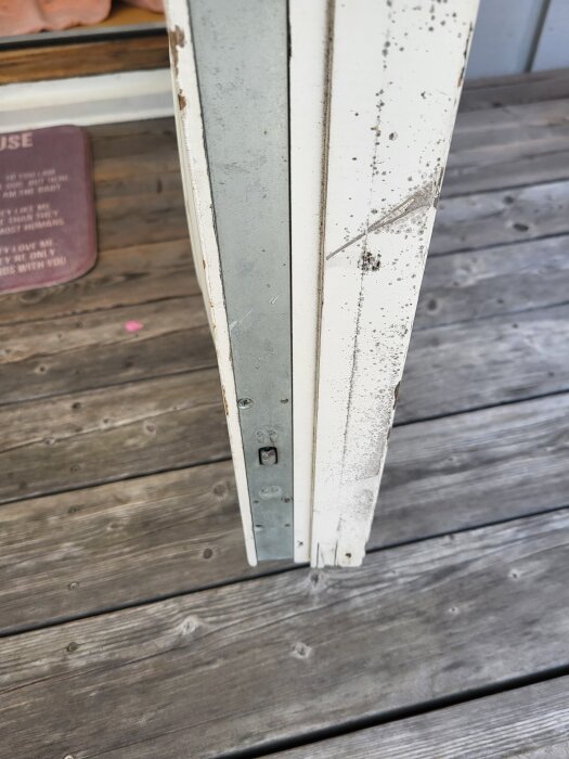 Närbild på kanten av en vit altandörr med slitage, stående på ett trädäck.