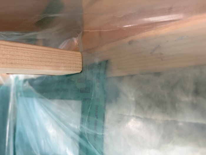 Träregel monterad i ett hörn mot en vägg, med plastfolie och isolering synliga i bakgrunden.