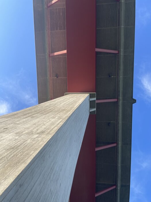 Betongpelare som stödjer en bro ovanifrån, med röd markering på brostrukturen och blå himmel i bakgrunden.