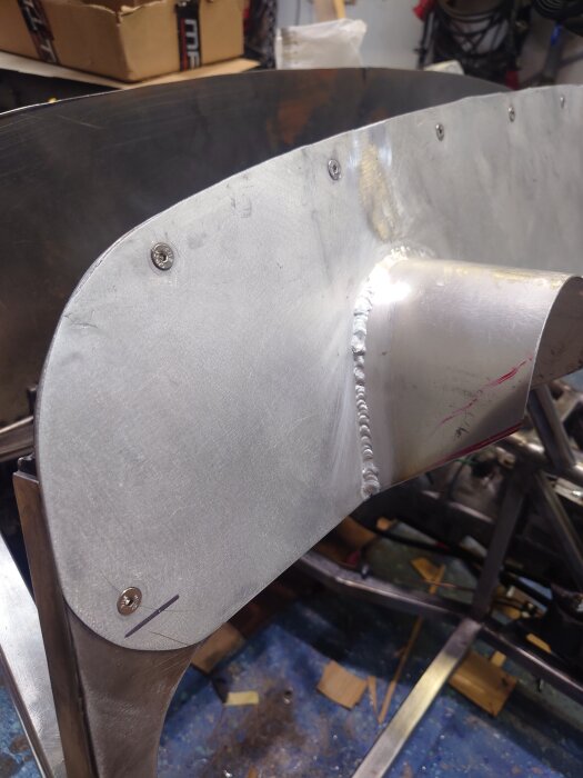 Instrumentpanel med ny fästplåt och svetsad remsa för scuttlen. Synliga skruvar och svetssöm på blanka metallplåtar i verkstadsmiljö.