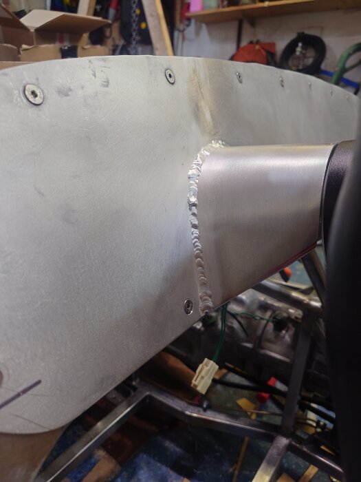 Metallpanel med svetsad fog och flera skruvade fästhål, del av ett byggprojekt för instrumentpanelen i ett fordon i en verkstadsmiljö.