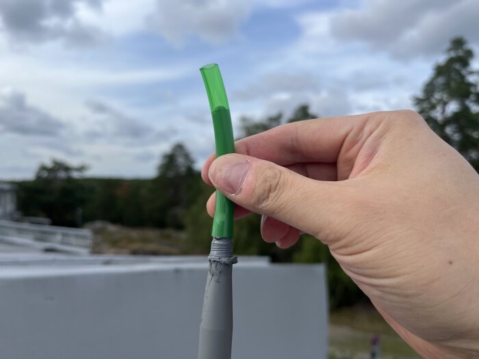 Hand håller i en grön slang mot en bakgrund av träd och himmel, förmodligen använd för byggrelaterade tester.