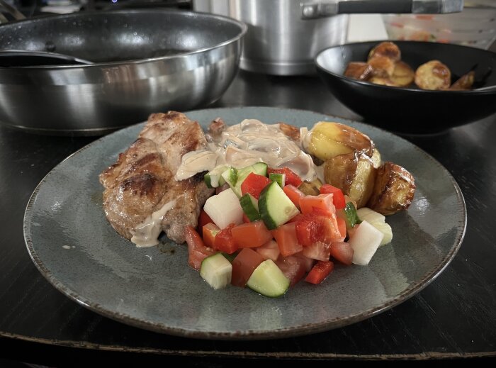 Fläskkarré med sås, ugnsstekt potatis och sallad på en tallrik.