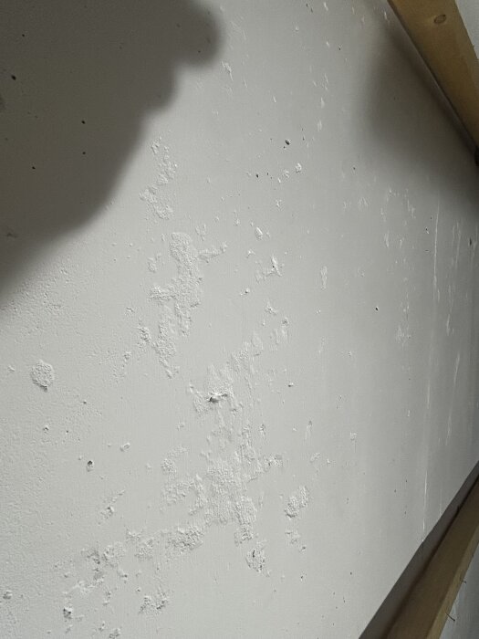 Vägg av lättbetong i källare med flagad puts och skuggor.