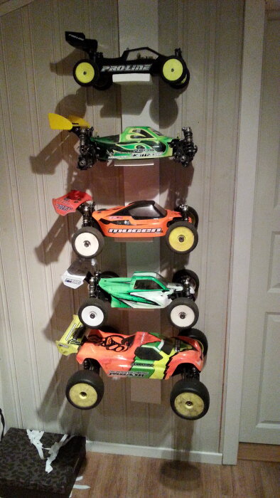 Fyra Mugen radiostyrda bilmodeller uppställda vertikalt på en vägg, inklusive buggy och truggy, med olika färgglada karosser.
