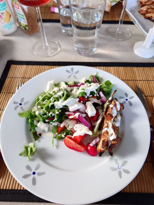 Tallrik med Ceasarsallad-variant innehållande sallad, tomat, rödlök och grillad kyckling med dressing.