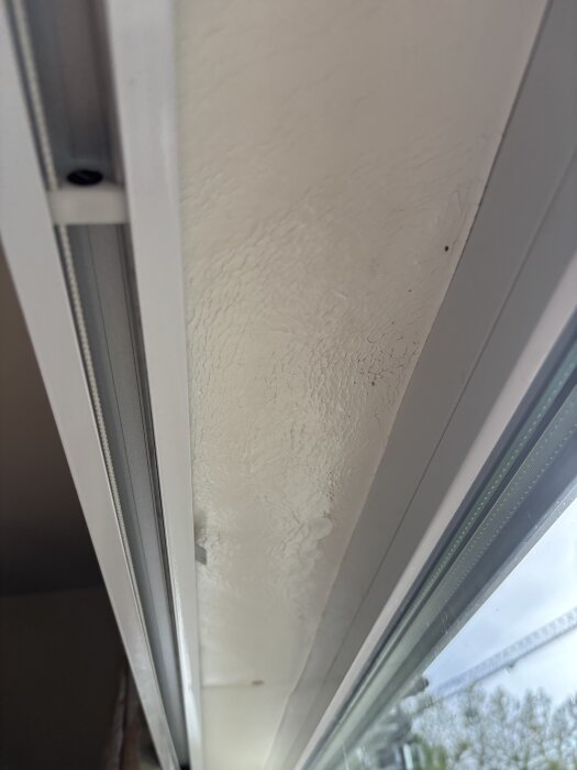 Svullet och blött foder ovanför ett fönster efter kraftigt regn, synligt från en inomhusvy nära fönstret.