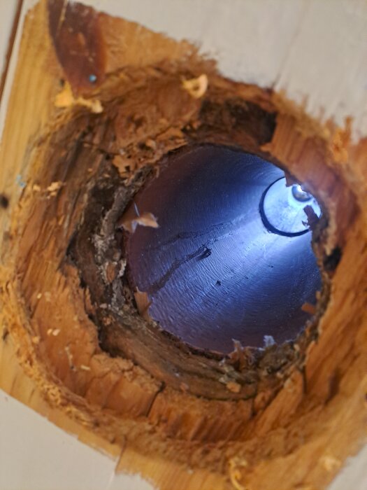 Närbild av ett oskarvat plaströr, delvis omgivet av trä, med synlig isolering och glipor runt rörets öppning.