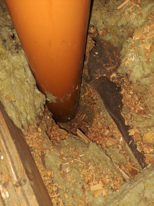 Orange plaströr på vind med kutterspån i isoleringen runtomkring, löst monterat vilket orsakar problem med ventilation och fukt.