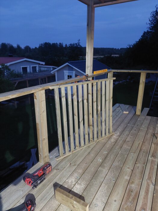 Träpergola under byggnation med nytt räcke på en altan, omgiven av trädgård och hus i bakgrunden, verktyg och överliggare synliga.