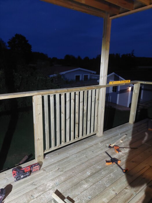 Träpergola med nybyggt räcke och överliggare kvällstid, verktyg ligger på trätrallen.