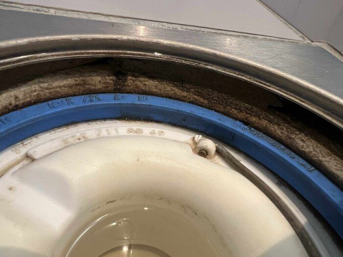 Närbild på en golvbrunn i ett badrum med blå och vita komponenter och smutsig omgivande kant i metall.