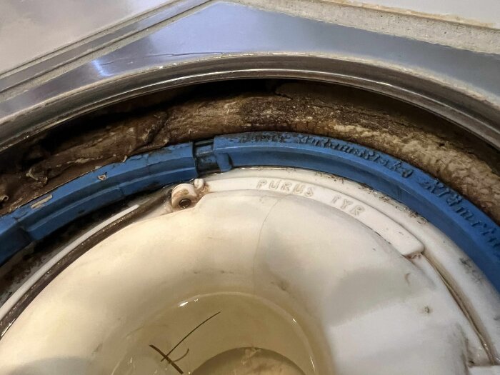 Golvbrunn i badrummet med blå tätning och synliga texturer; möjligt fogmassa eller lös manschett.