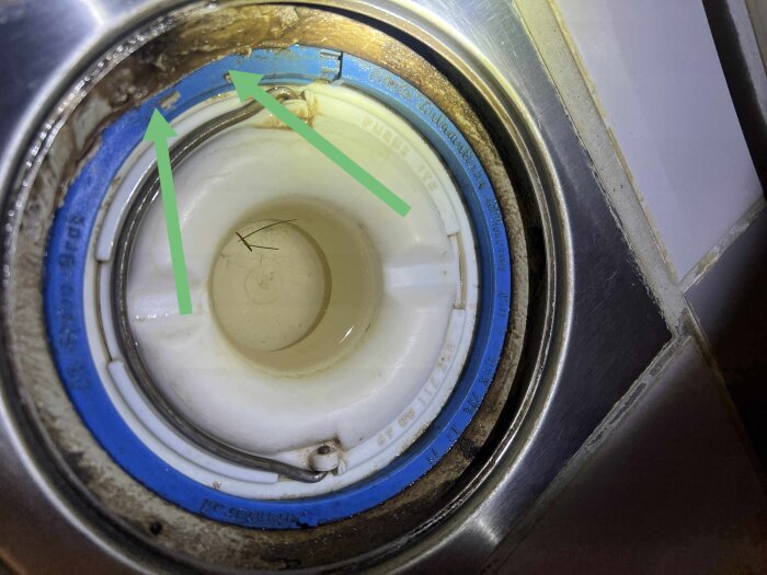 Golvbrunn i badrum med gröna pilar som pekar på brunnsmanchettens kanter och fogmassa runt brunnen.