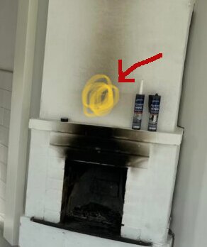 Eldstad målad med fläckar och sot, två burkar fogmassa på den. Röd pil pekar på eldstaden.