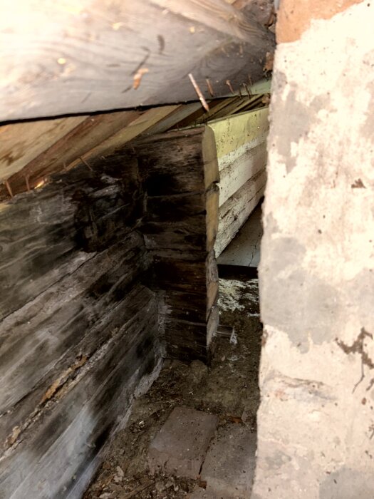 Rå träkonstruktion bakom murstock, visar slitage och potentiell instabilitet. Rustikt virke och tegel synliga, ev. tecken på fukt eller förfall.