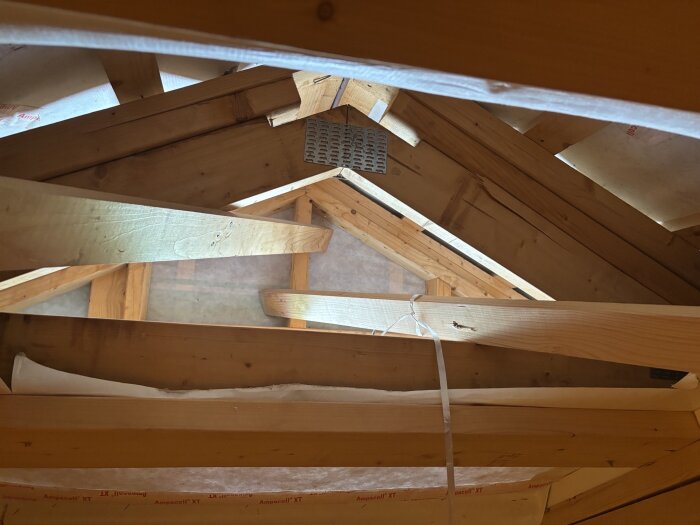 Takstolar och träbjälkar i en oisolerad vind med en öppning i väggen, del av en diskussion om ventilation och fuktighet i vindsutrymme.