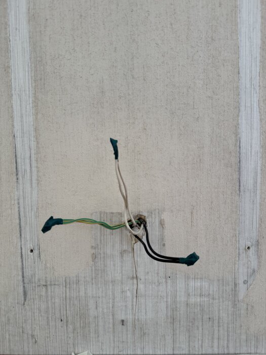 Kablar täckta med eltejp sticker ut från ett hål i en vägg där ett gammalt element suttit.