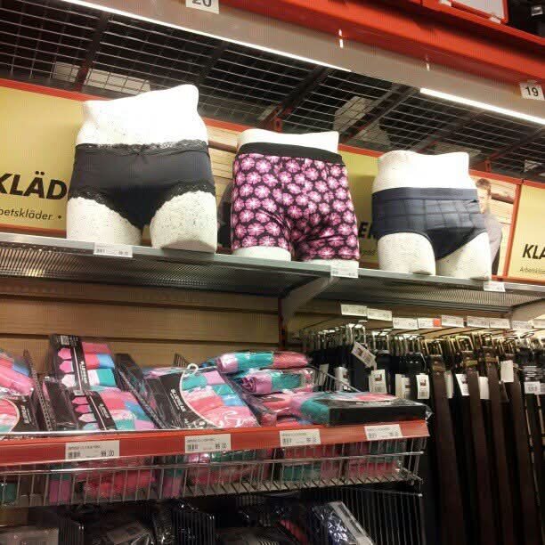 Underkläder visas på skyltdockor i butikshylla med paket med färgglada strumpor och skärp staplade nedanför.