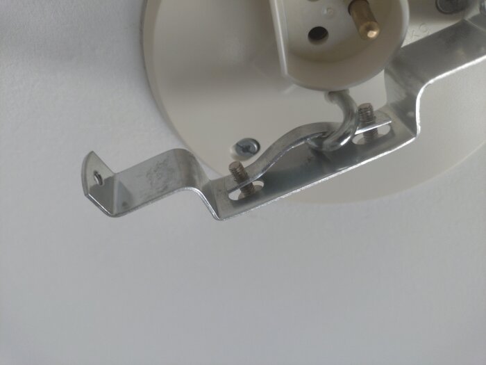 Metallfäste för lampkåpa med krok och öppning visas monterad i tak, med problem att passa ordentligt.