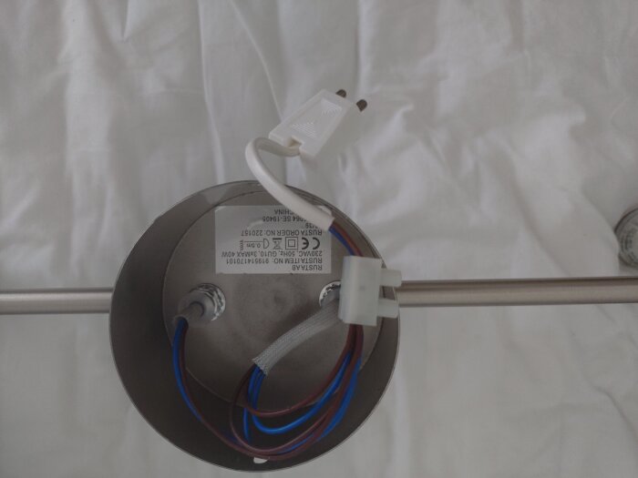 Lampfäste med kablar och kontakt, visar problem med att fästa lampkåpan på rätt sätt. En metallstav och etikett syns också.