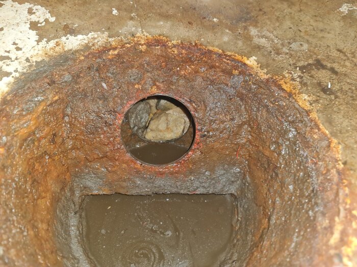 Rostigt avloppsrör i källare med makadam synligt inuti.
