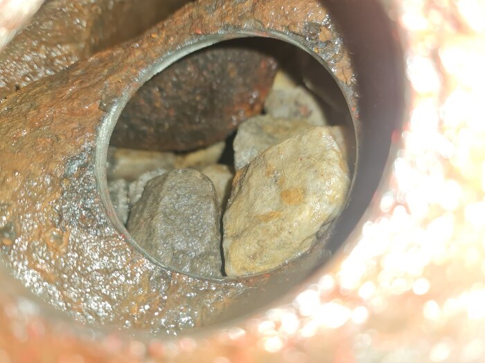 Bild av ett avloppsrör med makadam och stenar inuti. Rörväggen är av gjutjärn, och stenarna blockerar flödet.