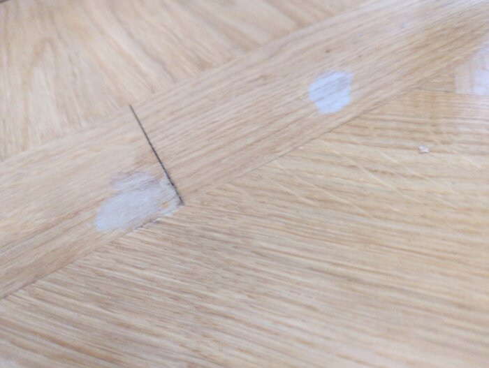 Lackskador på ett parkettgolv, två ljusa fläckar syns tydligt där ytmaterialet är skadat.