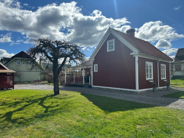 Rött småhus med vita knutar på en grön gräsmatta, molnig himmel i bakgrunden. Hus från 1924, Örebro, Sverige.